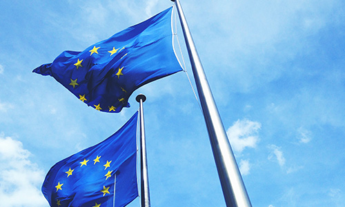 två EU-flaggor på flaggstång mot blå himmel