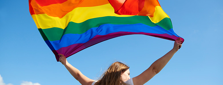 tjej som håller upp regnbågsflaggan mot himlen
