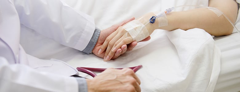 sjukhuspersonal som håller patient i handen i sjukhussäng