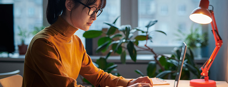 ung kvinna som använder laptop, med en skrivbordslampa tänd bredvid